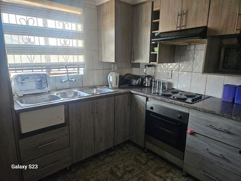Functional kitchen featuring wood-look laminate cabinetry, built-in oven and hob, tiled backsplash, and a double sink with security bars on the window.