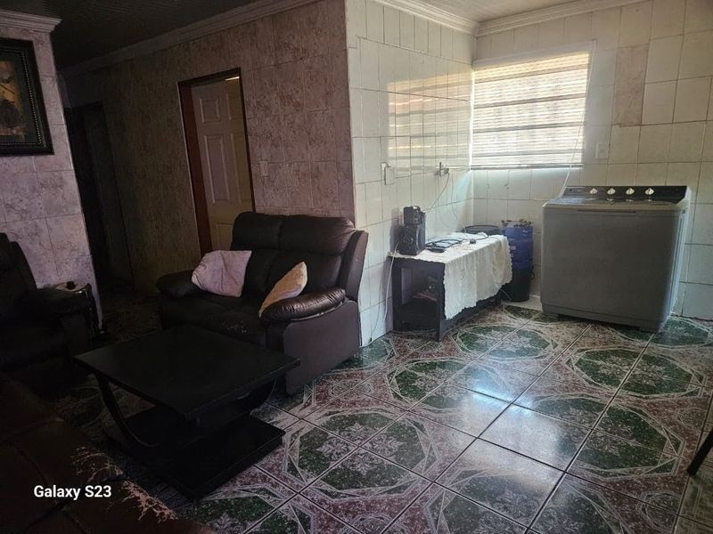 Open plan living area featuring tiled flooring and wall cladding, providing a functional space with potential for modern updates.