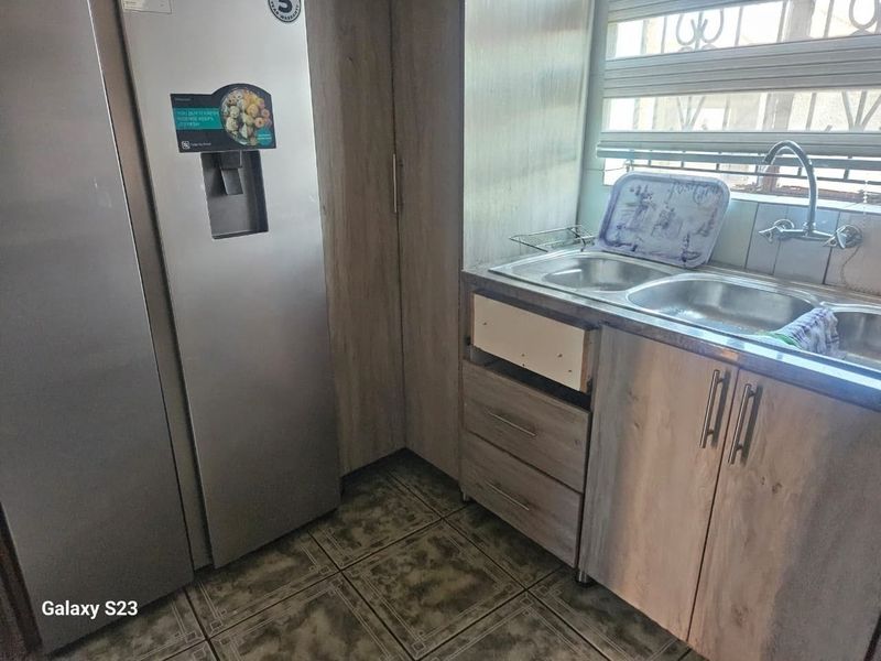 A functional kitchen area featuring laminate cabinetry, a double bowl stainless steel sink, and tiled flooring, currently requiring minor repairs to cabinetry.