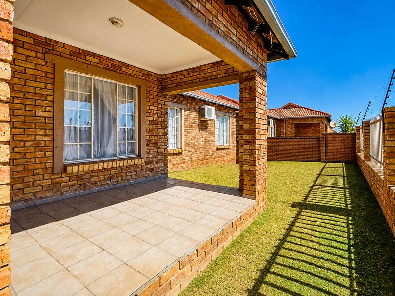 A covered brick patio overlooking a private garden area, featuring tiled flooring and secure perimeter walling with electric fencing.