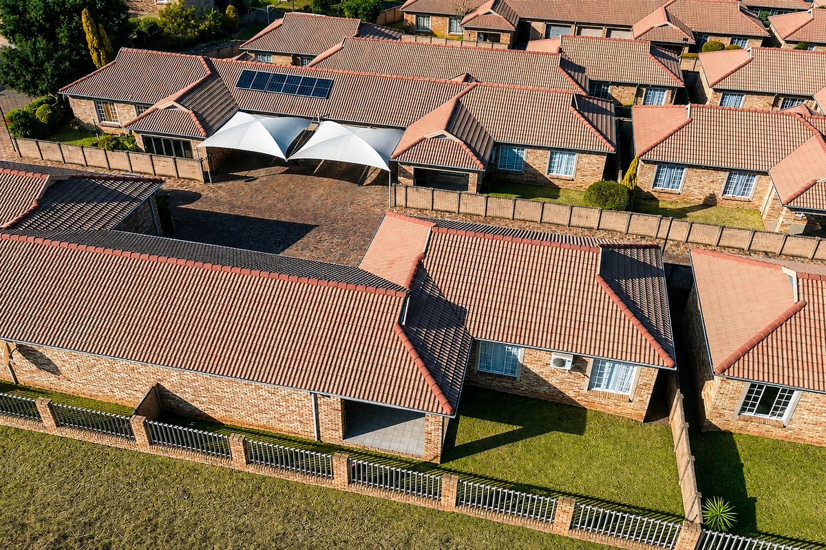 Aerial view of a townhouse complex featuring brick construction, tiled roofs, solar panels, paved driveways, and private garden areas.