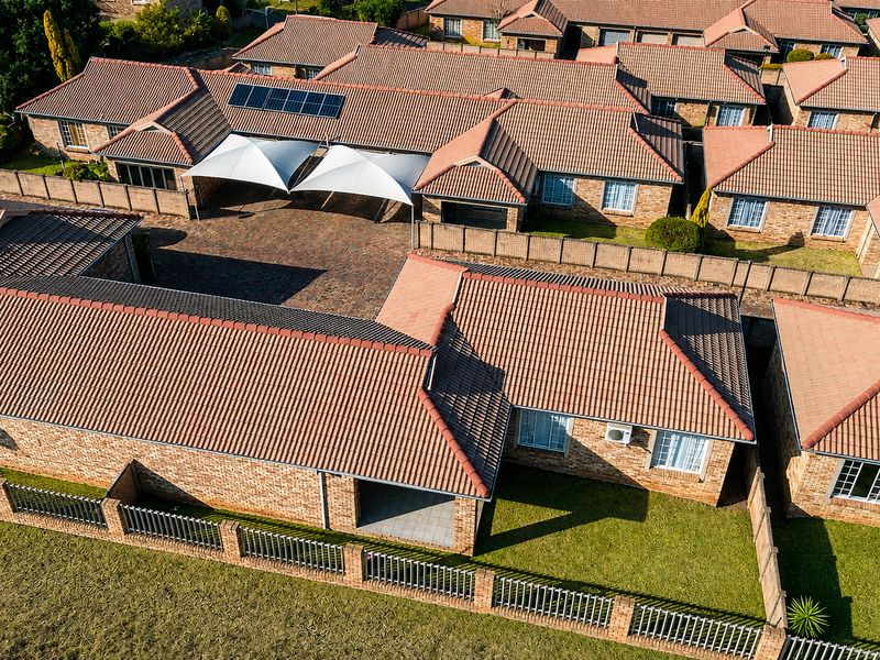 Aerial view of a townhouse complex featuring brick construction, tiled roofs, solar panels, paved driveways, and private garden areas.