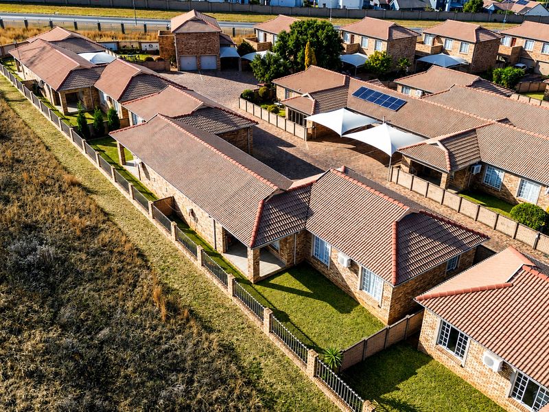 Aerial view of a townhouse complex featuring brick construction, tiled roofs, paved driveways, and private garden areas with shade sails.