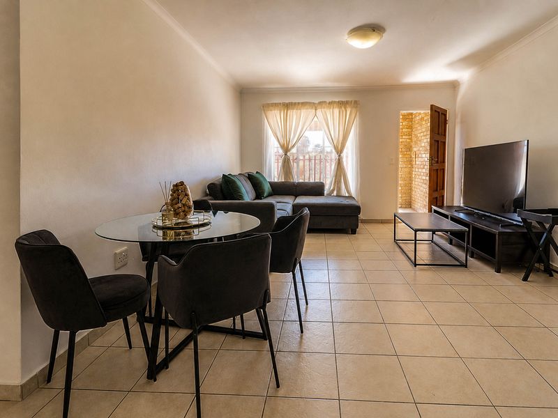 A functional open-plan living and dining area featuring neutral tiled flooring and access to an exterior space.
