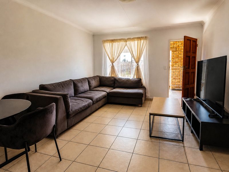 A living room featuring ceramic floor tiles, coved ceilings, and direct access to an outdoor area through a timber door.