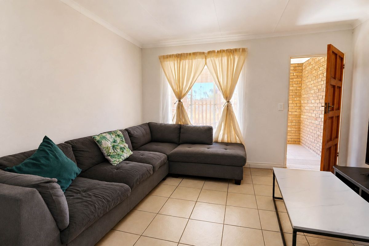 A bright living room featuring neutral tiled flooring, cove cornicing, and direct access to an exterior brick-walled patio area.