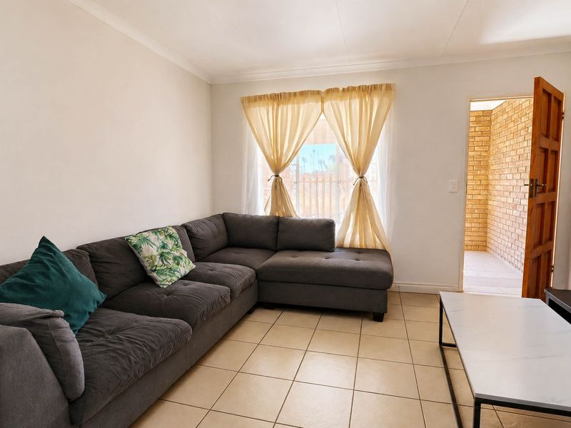 A bright living room featuring neutral tiled flooring, cove cornicing, and direct access to an exterior brick-walled patio area.