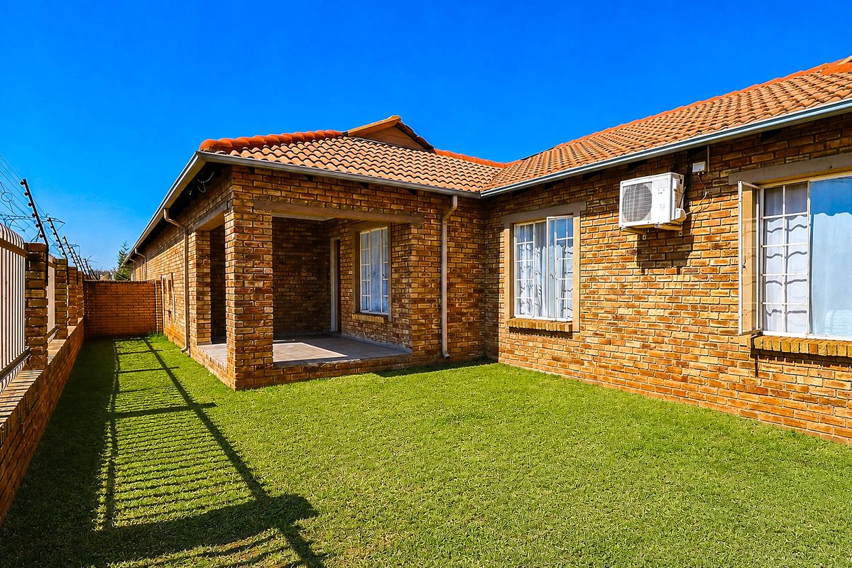 Rear view of the townhouse featuring a face brick facade, a covered patio area, and a private garden with perimeter electric fencing.