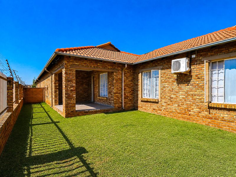Rear view of the townhouse featuring a face brick facade, a covered patio area, and a private garden with perimeter electric fencing.