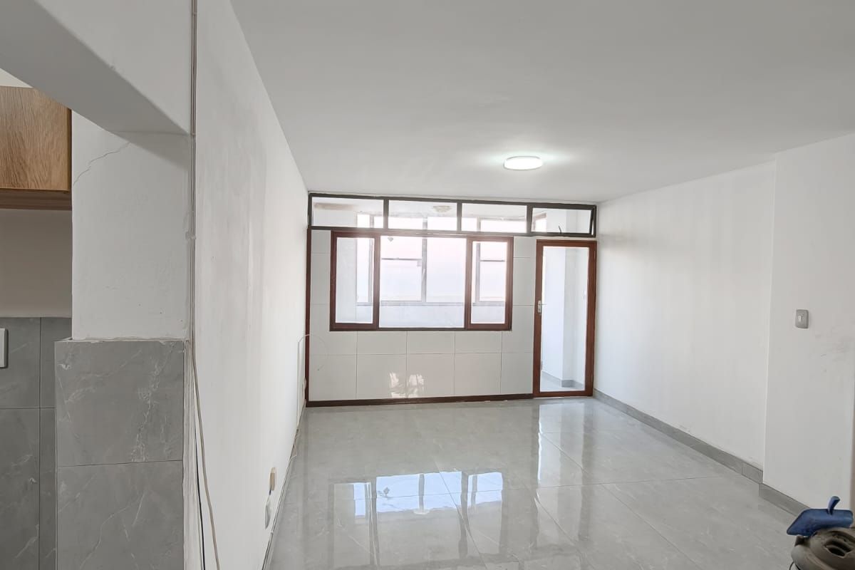 An empty open-plan living area featuring large windows, a glass door, and polished grey floor tiles, awaiting final finishes and interior styling.