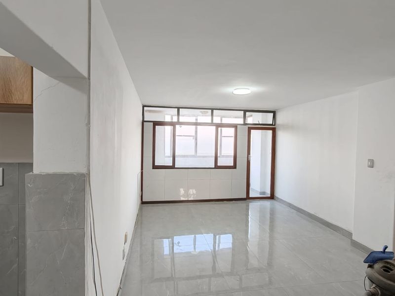 An empty open-plan living area featuring large windows, a glass door, and polished grey floor tiles, awaiting final finishes and interior styling.