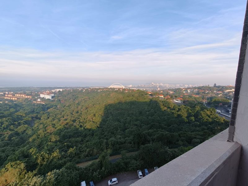 Elevated panoramic view overlooking a lush green landscape and distant city skyline from a balcony.