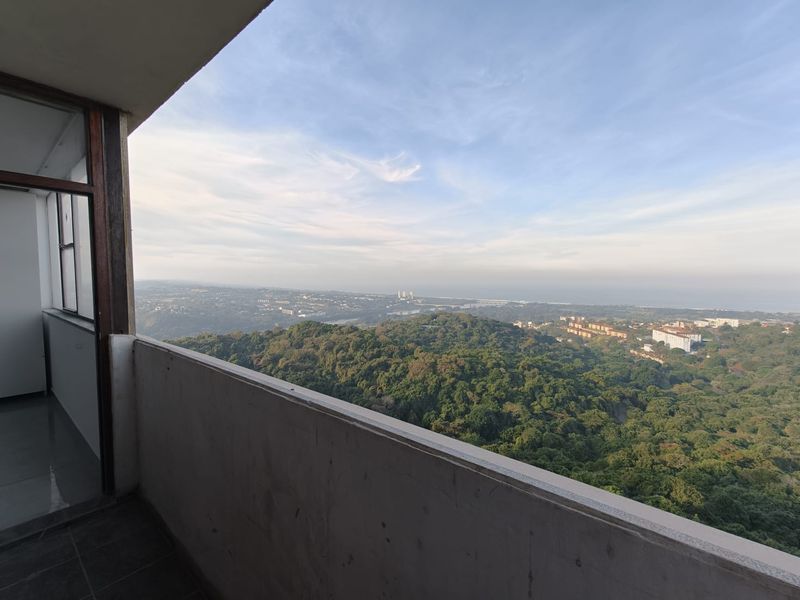 A balcony featuring a concrete balustrade and tiled flooring, offering expansive elevated views over the surrounding landscape and distant coastline.