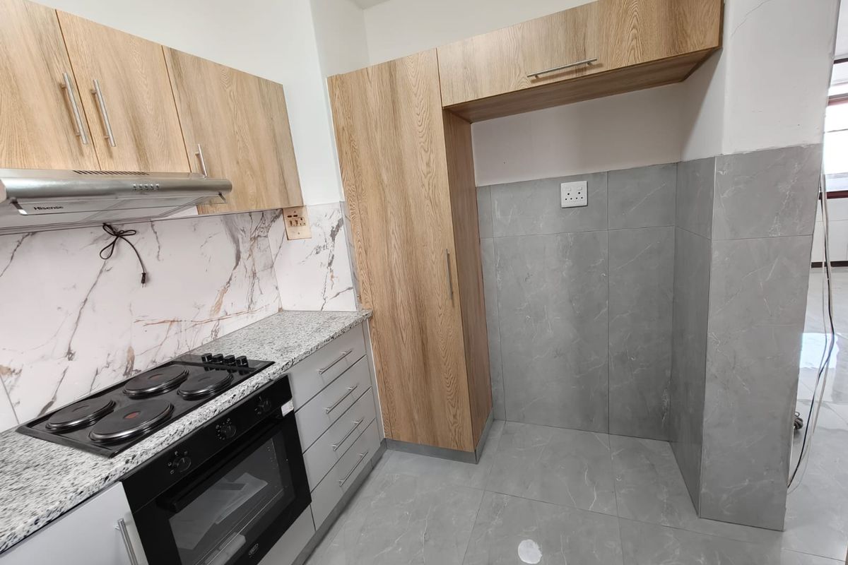 Modern kitchen featuring light wood-look cabinetry, granite countertops, built-in oven and hob, and grey tiled flooring with a marble-effect backsplash.