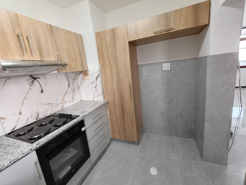 Modern kitchen featuring light wood-look cabinetry, granite countertops, built-in oven and hob, and grey tiled flooring with a marble-effect backsplash.