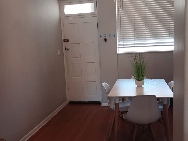 A bright dining area featuring polished hardwood flooring, crown molding, and a classic panelled entrance door with a transom window.