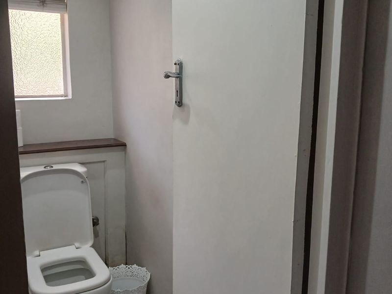 A compact bathroom featuring a standard toilet, recessed ceiling lighting, and a window with a fitted blind.
