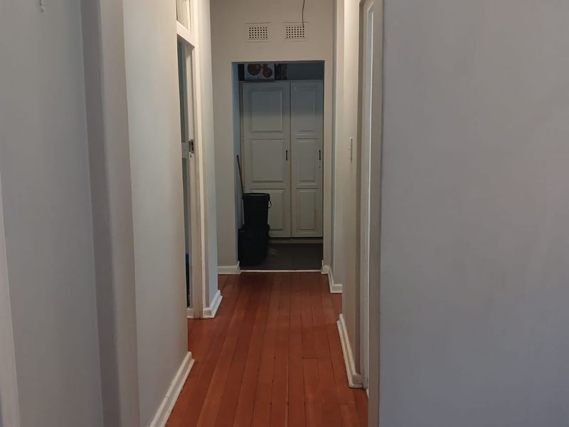 A clean, empty hallway featuring polished hardwood flooring, neutral walls, and a built-in storage cupboard at the end.