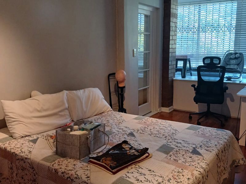 Bedroom featuring hardwood flooring, an exposed brick accent pillar, and a glass-paneled door leading to an adjacent space with large windows.