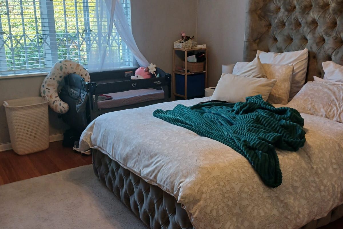 A well-maintained bedroom featuring laminate flooring, crown molding, an integrated air conditioning unit, and a large window with security bars and blinds.