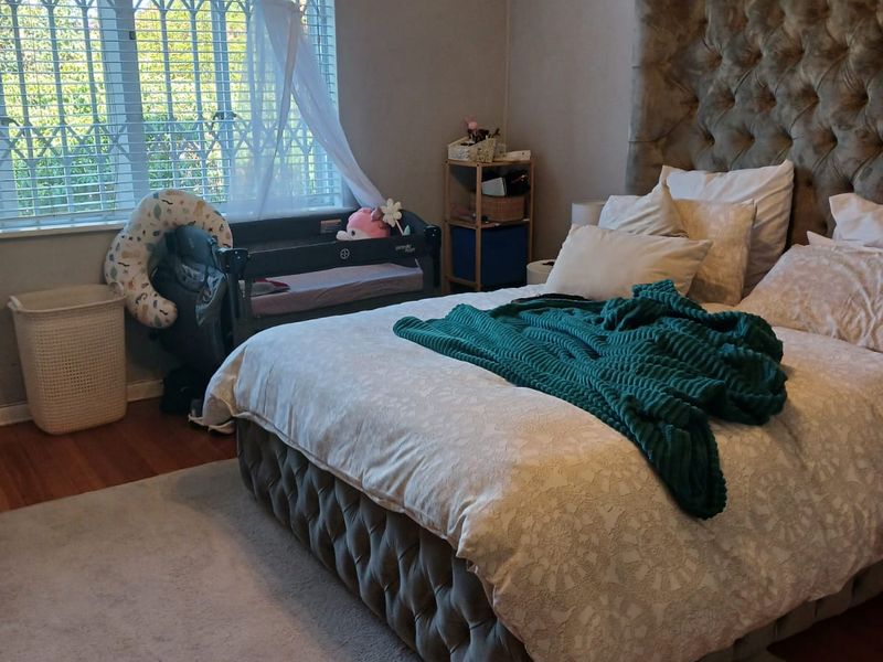 A well-maintained bedroom featuring laminate flooring, crown molding, an integrated air conditioning unit, and a large window with security bars and blinds.
