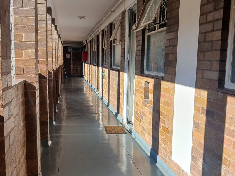 An exterior apartment building walkway featuring exposed brick walls, structural brick pillars, and painted concrete flooring with access to multiple units.