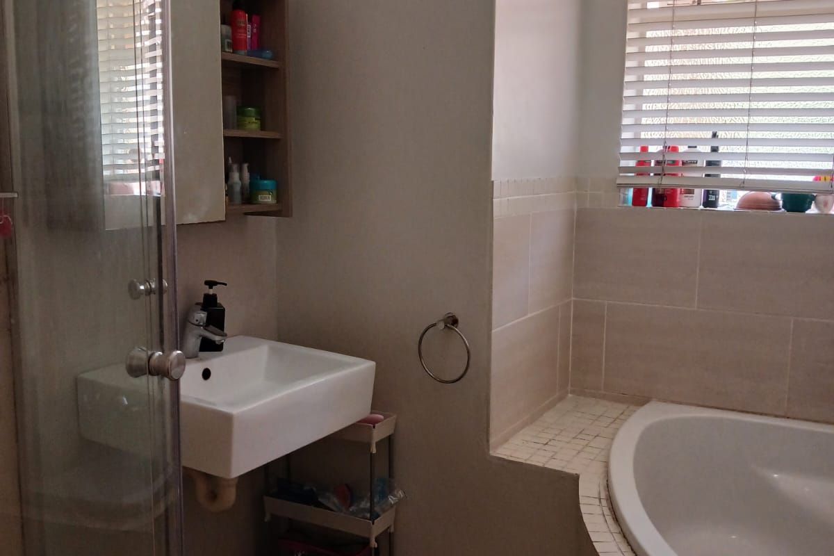 A functional bathroom featuring a built-in bathtub, a separate glass shower enclosure, and a wall-mounted basin with tiled finishes.