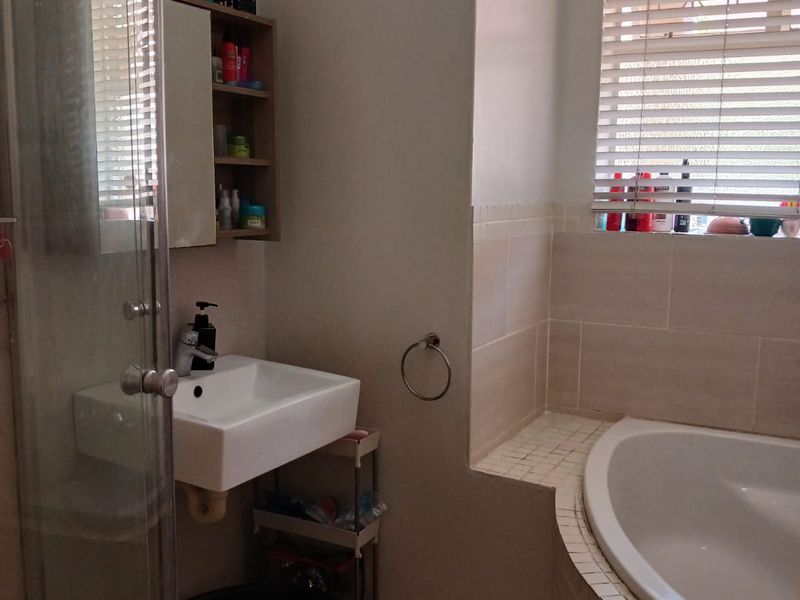 A functional bathroom featuring a built-in bathtub, a separate glass shower enclosure, and a wall-mounted basin with tiled finishes.