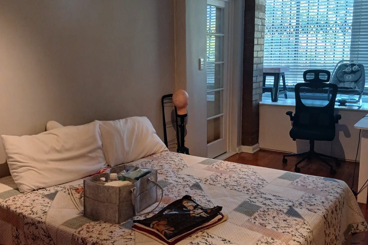 Bedroom featuring hardwood flooring, an exposed brick accent pillar, and a glass-paneled door leading to an adjacent space with large windows.