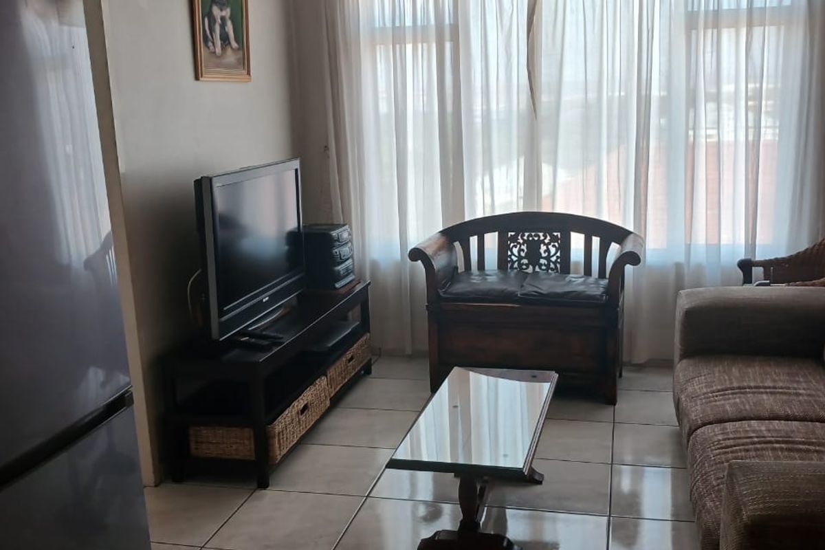 A functional living room featuring tiled flooring, a ceiling fan, and large windows that provide natural light.