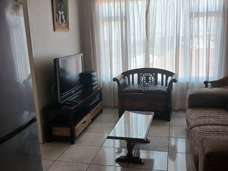 A functional living room featuring tiled flooring, a ceiling fan, and large windows that provide natural light.