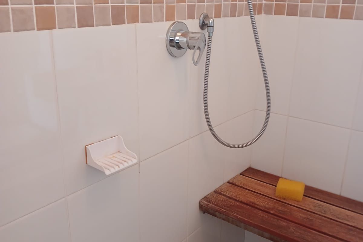 A functional shower enclosure featuring a built-in wooden bench, chrome shower fixtures, and neutral ceramic wall tiling.