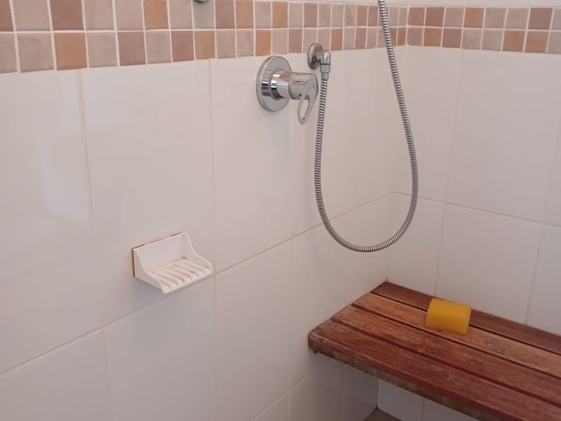 A functional shower enclosure featuring a built-in wooden bench, chrome shower fixtures, and neutral ceramic wall tiling.