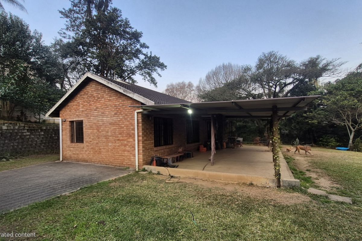 Rear view of a brick house featuring a covered patio area, concrete driveway, and a spacious garden setting.