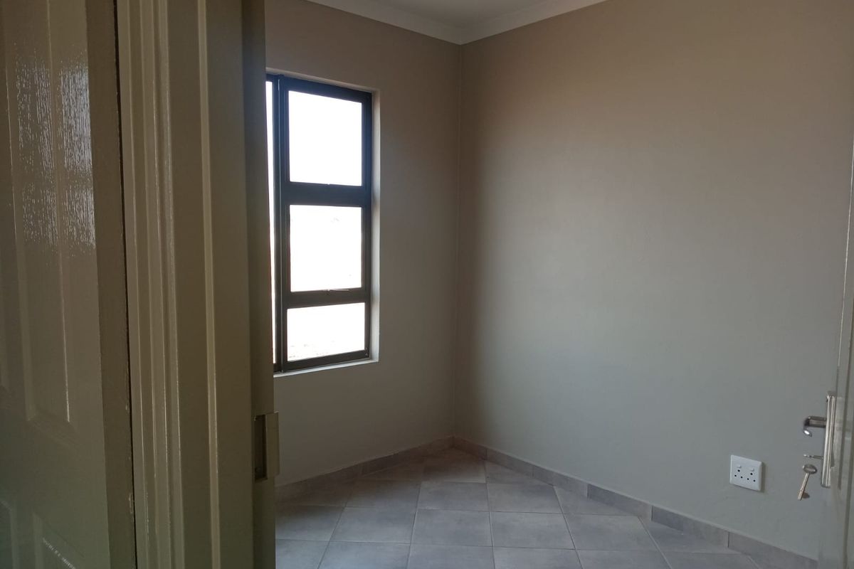 A clean, empty bedroom featuring neutral wall paint, tiled flooring, and an aluminium-framed window, providing a blank canvas for interior design.