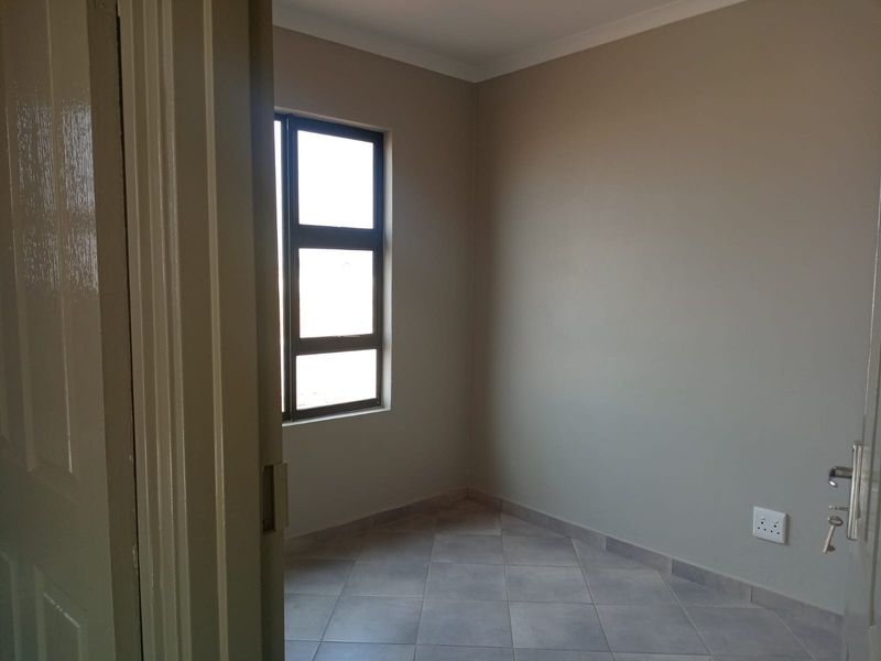 A clean, empty bedroom featuring neutral wall paint, tiled flooring, and an aluminium-framed window, providing a blank canvas for interior design.