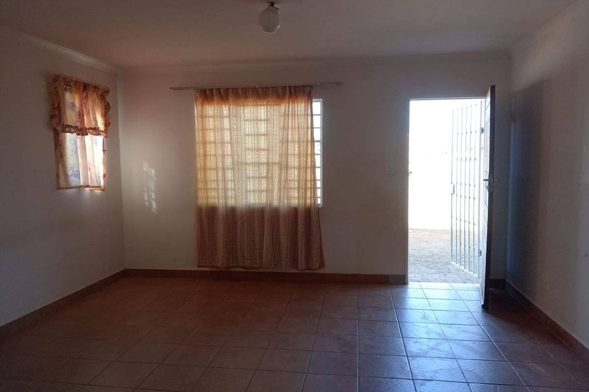 An empty living room featuring tiled flooring, a security gate at the entrance, and natural light from the windows.
