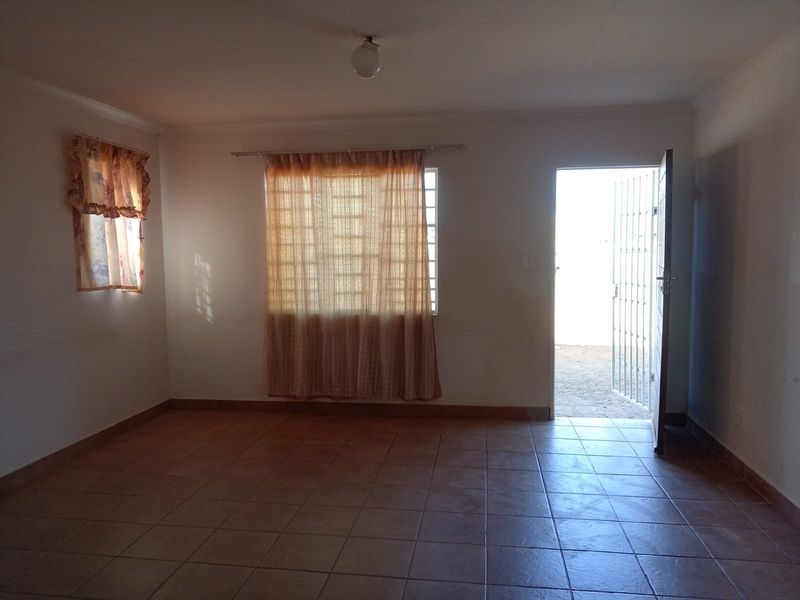 An empty living room featuring tiled flooring, a security gate at the entrance, and natural light from the windows.