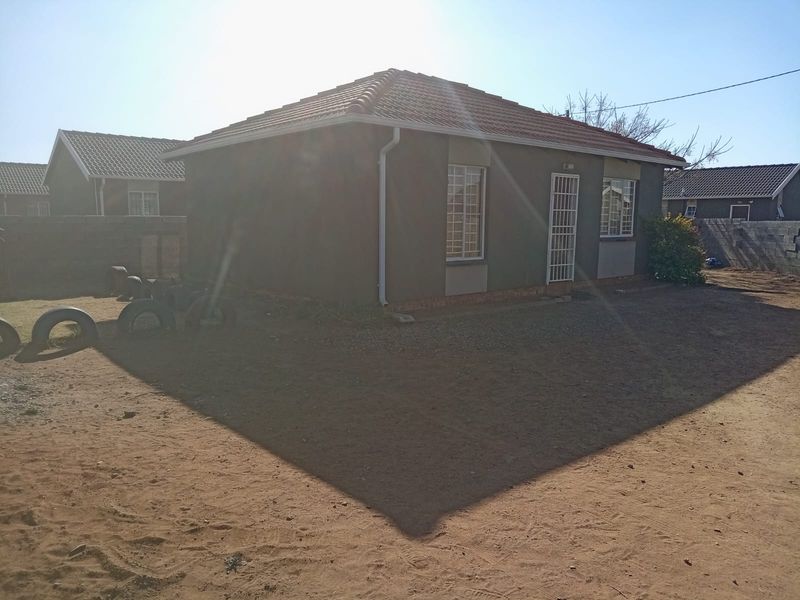 Rear view of a detached house featuring a tiled roof, security bars on windows, and a large, unlandscaped yard area.
