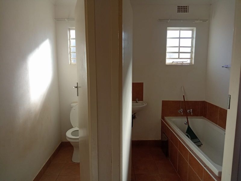 A functional bathroom featuring a separate toilet area, a bathtub with tiled surround, and a wall-mounted washbasin, requiring cosmetic updates.