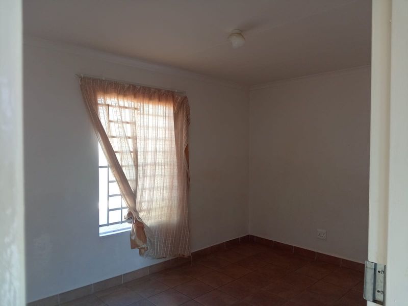 A simple, empty bedroom featuring tiled flooring, a window with security bars, and neutral wall finishes.