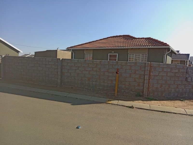 A view of the front exterior of a residential house featuring a tiled roof and a concrete block boundary wall.