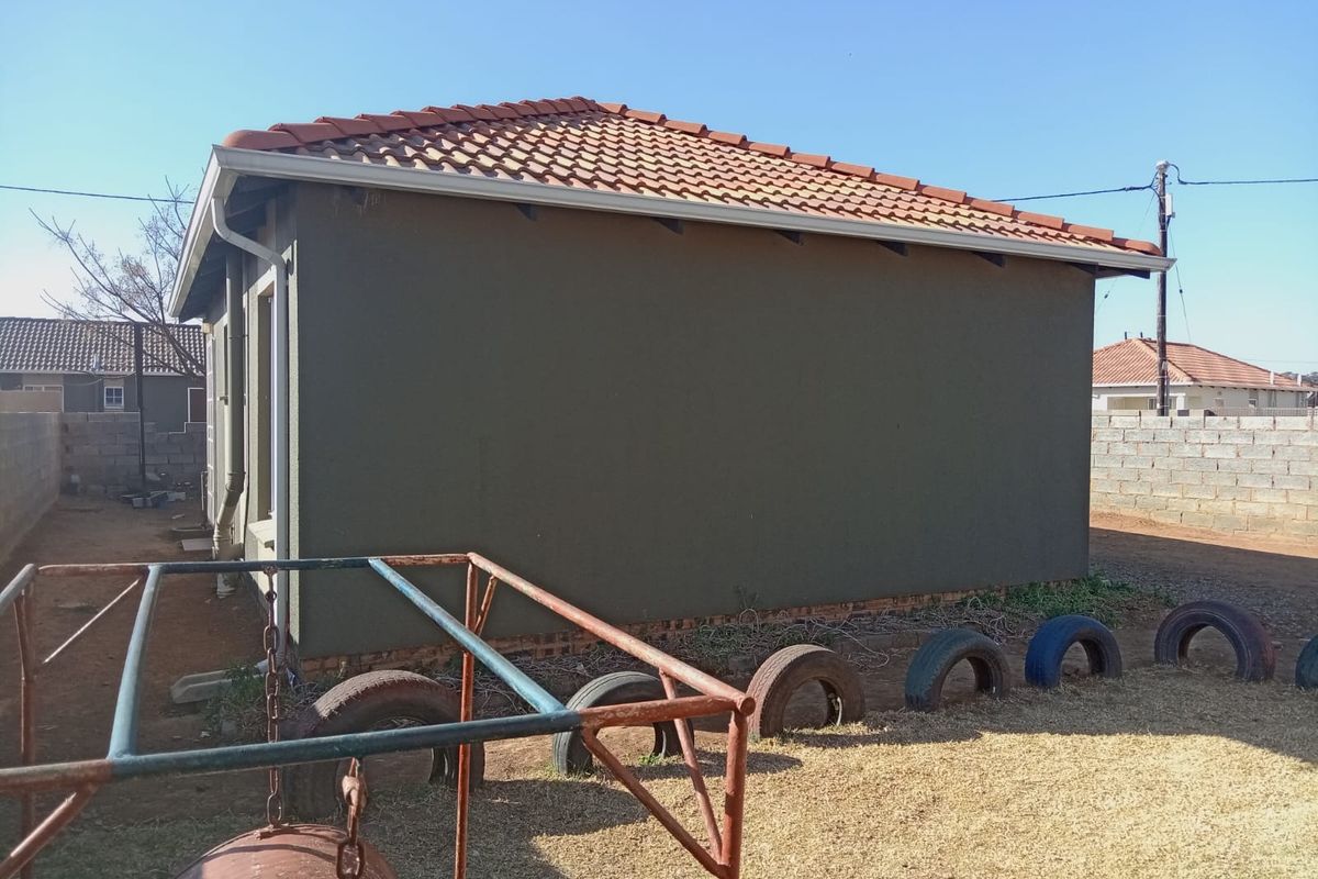 Rear view of the property showing the plastered exterior walls, tiled roof, and surrounding brick boundary wall.