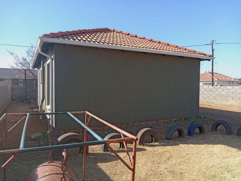 Rear view of the property showing the plastered exterior walls, tiled roof, and surrounding brick boundary wall.