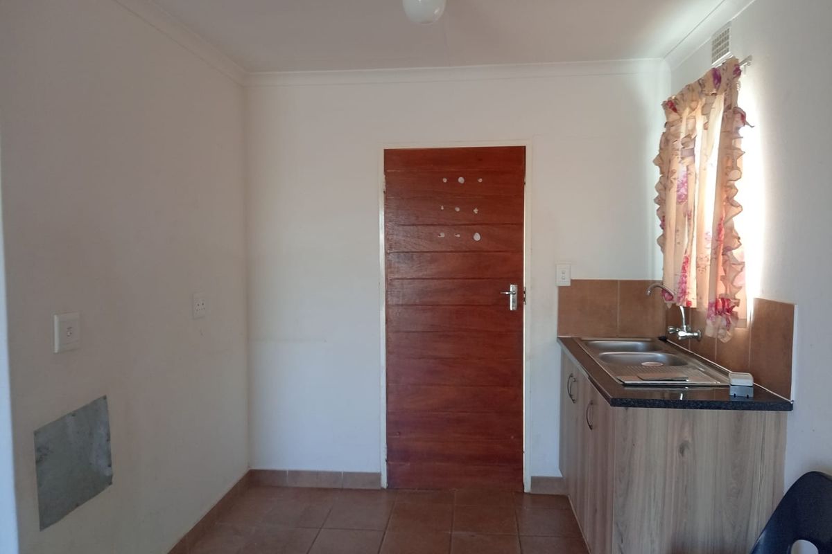 A compact kitchen area featuring tiled flooring, a single sink unit with laminate cabinetry, and a tiled splashback.
