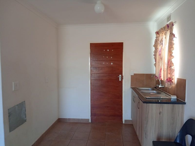 A compact kitchen area featuring tiled flooring, a single sink unit with laminate cabinetry, and a tiled splashback.