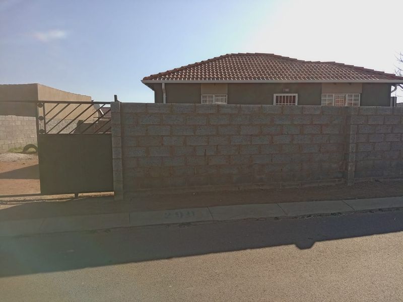 Front view of the property featuring a tiled roof house, secured by a perimeter wall and metal gate.