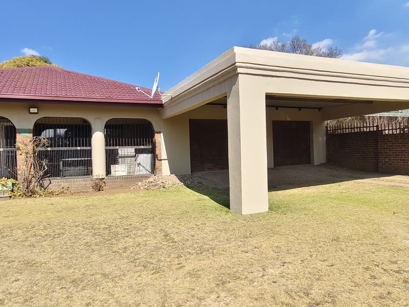 Front exterior view featuring a spacious carport, double garage doors, and a covered arched veranda with security gates.