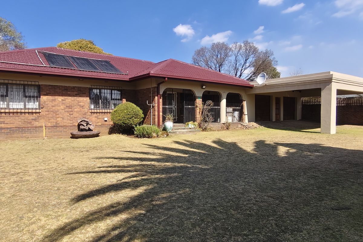 Rear view of a brick house featuring a tiled roof with solar panels, a spacious lawn, and an attached carport.