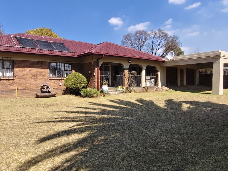Rear view of a brick house featuring a tiled roof with solar panels, a spacious lawn, and an attached carport.